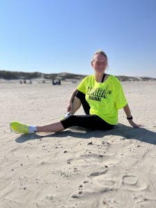 Die Zumba-Instructorin Kerstin Steinkamp sitzt am fast menschenleeren Strand im neonfarbenen Zumba-Outfit im hellen Sand